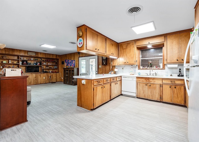 kitchen featuring white appliances, wooden walls, kitchen peninsula, and sink