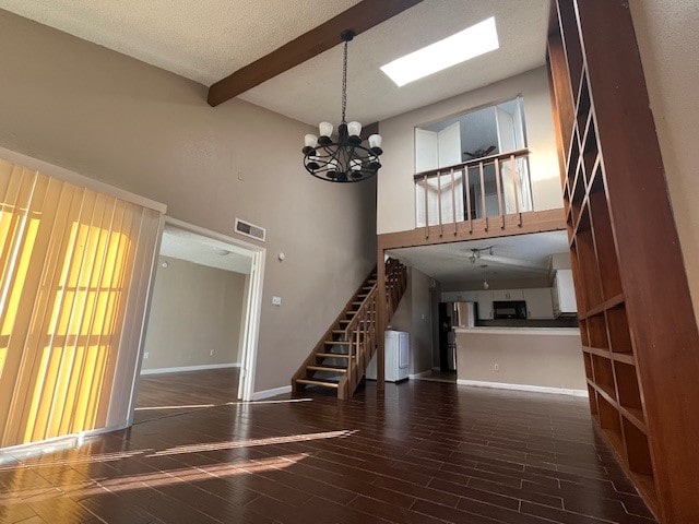 unfurnished living room with a high ceiling, beamed ceiling, dark hardwood / wood-style flooring, a chandelier, and a skylight