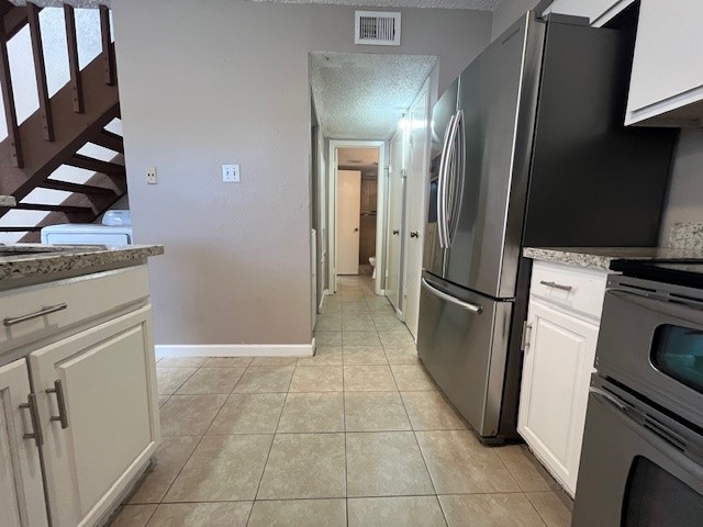 kitchen with appliances with stainless steel finishes, white cabinets, a textured ceiling, and light tile patterned floors