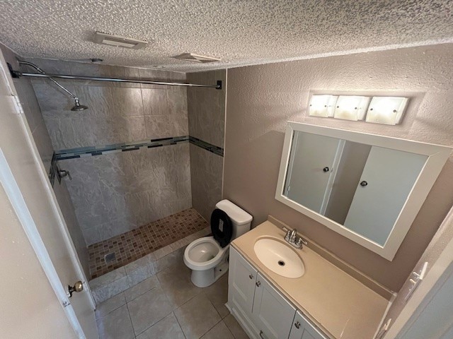 bathroom with tile patterned floors, toilet, vanity, a tile shower, and a textured ceiling