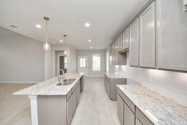 kitchen with sink, a center island with sink, tasteful backsplash, and gray cabinetry