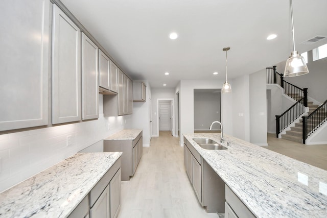 kitchen featuring hanging light fixtures, light hardwood / wood-style flooring, sink, and light stone countertops