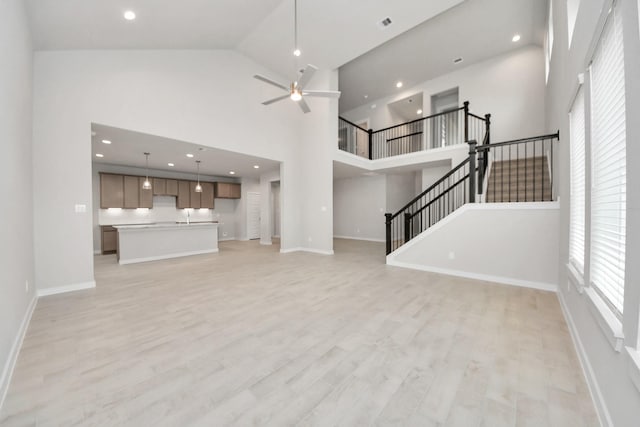 unfurnished living room with ceiling fan, high vaulted ceiling, and light wood-type flooring