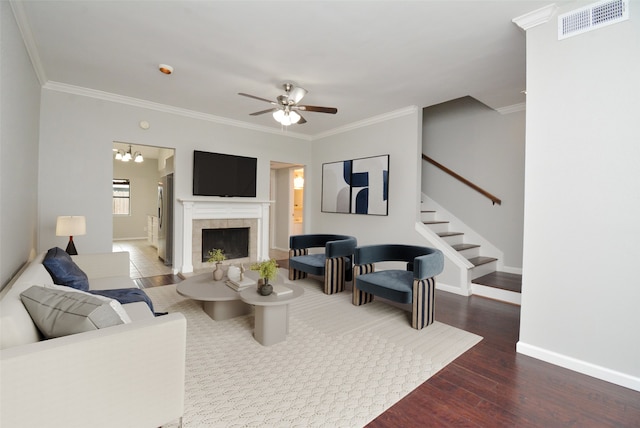 living room featuring crown molding, a tiled fireplace, dark hardwood / wood-style floors, and ceiling fan with notable chandelier