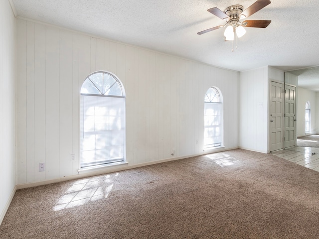 spare room with ceiling fan, wood walls, a textured ceiling, and light colored carpet