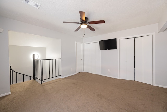 interior space with ceiling fan, a textured ceiling, multiple closets, and carpet floors