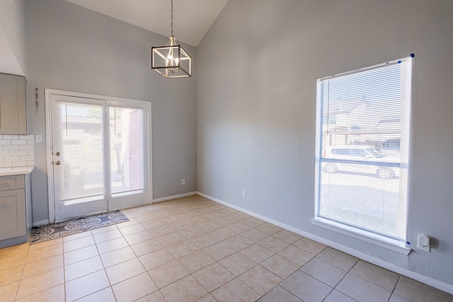 unfurnished dining area with an inviting chandelier, light tile patterned flooring, and high vaulted ceiling