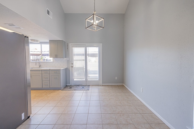 kitchen with hanging light fixtures, light tile patterned floors, high vaulted ceiling, stainless steel refrigerator, and sink