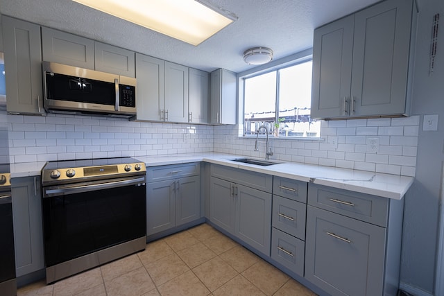 kitchen featuring decorative backsplash, stove, light tile patterned flooring, gray cabinets, and sink