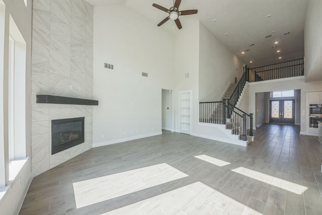 unfurnished living room featuring a towering ceiling, built in features, a tile fireplace, ceiling fan, and hardwood / wood-style flooring