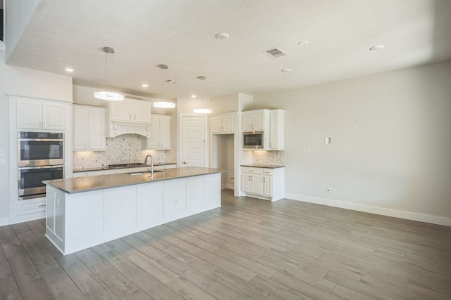 kitchen featuring a kitchen island with sink, light hardwood / wood-style flooring, hanging light fixtures, stainless steel appliances, and white cabinets