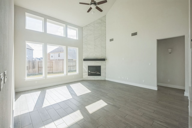 unfurnished living room with hardwood / wood-style floors, high vaulted ceiling, a tile fireplace, and ceiling fan