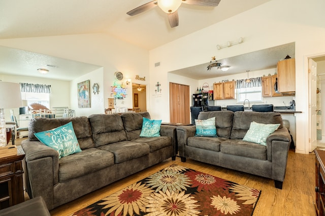 living room with sink, ceiling fan, vaulted ceiling, and light wood-type flooring