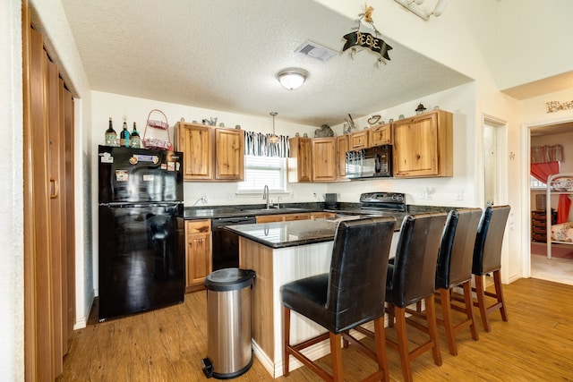 kitchen featuring a kitchen breakfast bar, light hardwood / wood-style flooring, decorative light fixtures, and black appliances