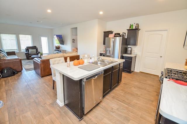 kitchen with appliances with stainless steel finishes, a kitchen island with sink, sink, and light wood-type flooring