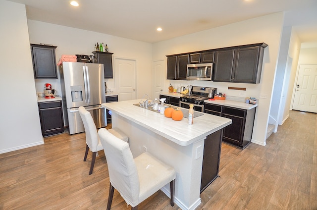 kitchen with dark brown cabinetry, stainless steel appliances, a center island with sink, and light wood-type flooring