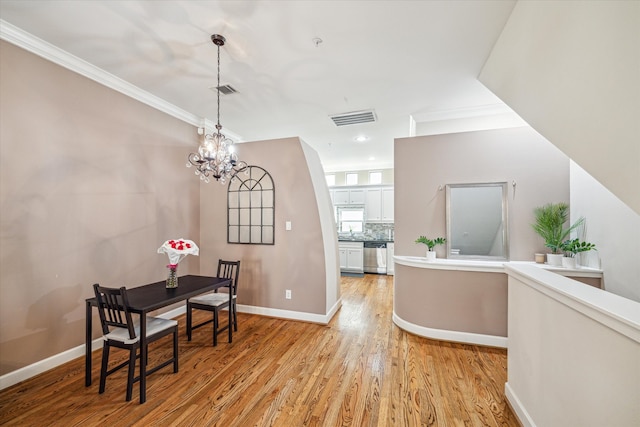 dining room with a notable chandelier, light wood-type flooring, and crown molding