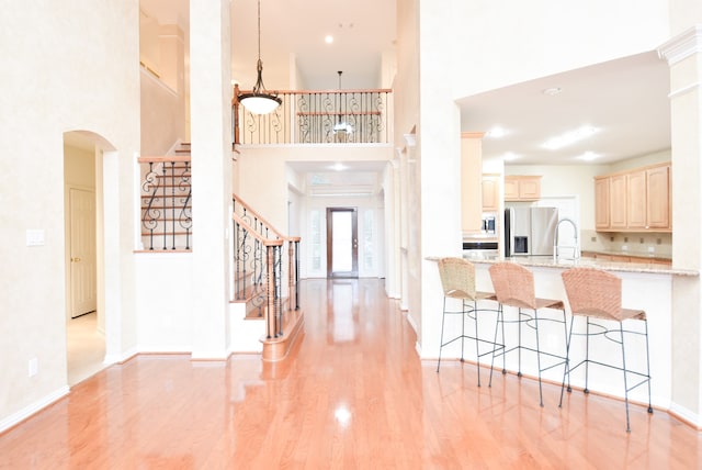 entrance foyer with sink, light hardwood / wood-style flooring, a towering ceiling, and decorative columns