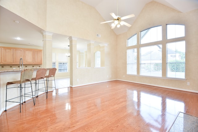 living room featuring ceiling fan, high vaulted ceiling, decorative columns, and light wood-type flooring