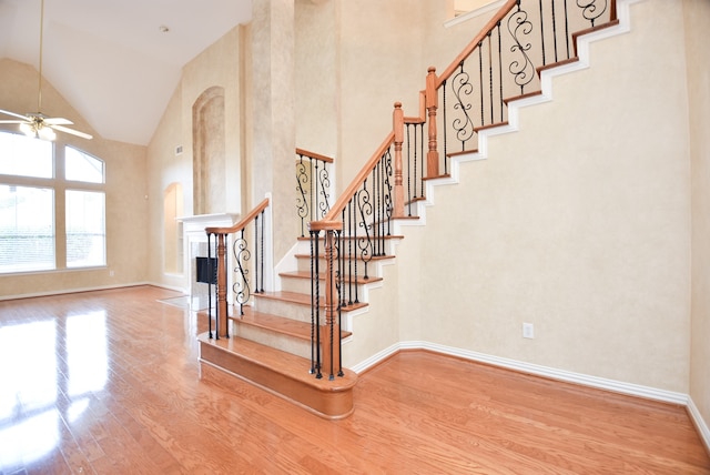 stairs with hardwood / wood-style flooring, high vaulted ceiling, and ceiling fan