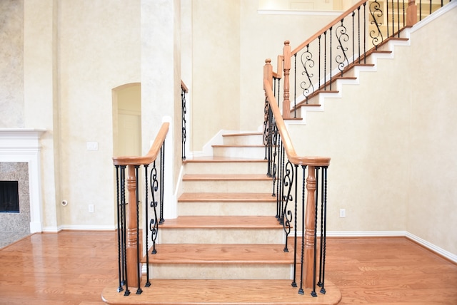 stairs featuring a towering ceiling, hardwood / wood-style floors, and a tiled fireplace