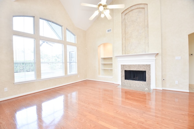 unfurnished living room with light hardwood / wood-style floors, built in shelves, high vaulted ceiling, and ceiling fan