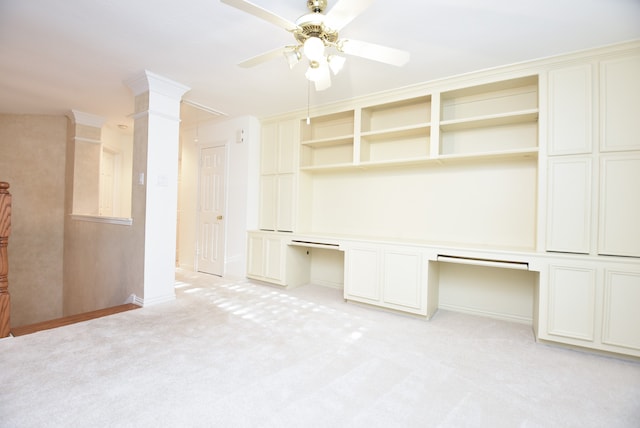 interior space with built in desk, decorative columns, light colored carpet, and ceiling fan