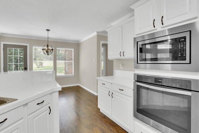 kitchen with appliances with stainless steel finishes, an inviting chandelier, white cabinetry, ornamental molding, and dark hardwood / wood-style floors