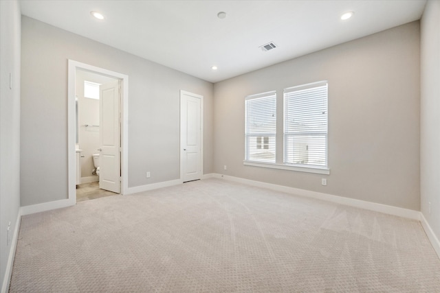 unfurnished bedroom with ensuite bath, light carpet, and a closet