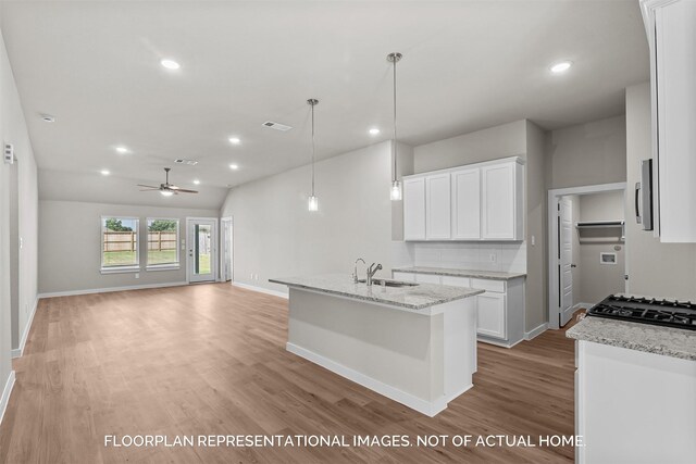 kitchen featuring white cabinetry, tasteful backsplash, a kitchen island with sink, ceiling fan, and light stone counters