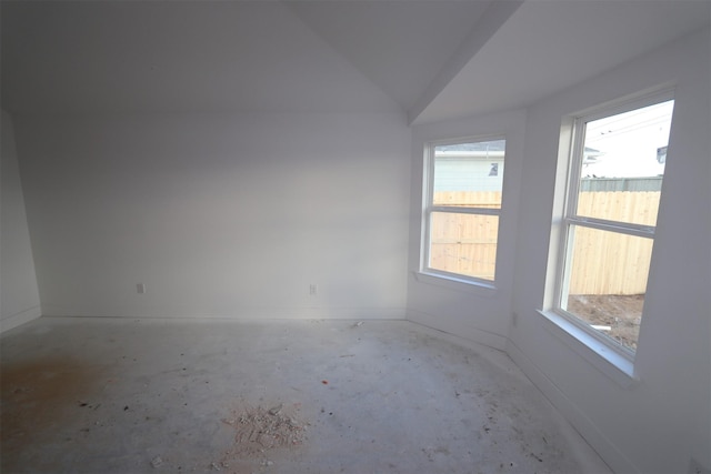 empty room with concrete floors, vaulted ceiling, and a healthy amount of sunlight