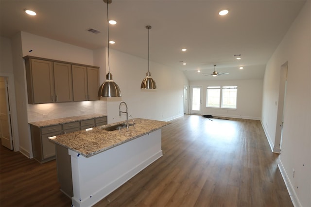 kitchen featuring dark hardwood / wood-style floors, an island with sink, sink, hanging light fixtures, and light stone countertops