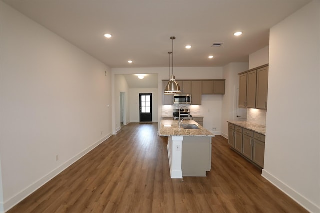 kitchen featuring a kitchen island with sink, dark wood-style flooring, hanging light fixtures, decorative backsplash, and stainless steel microwave