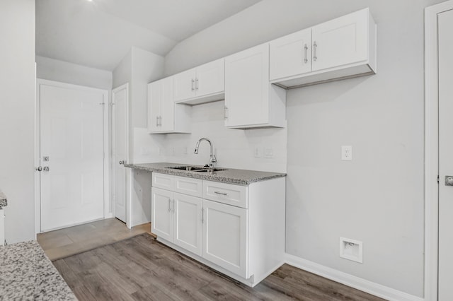 kitchen with sink, vaulted ceiling, white cabinets, light stone counters, and light hardwood / wood-style floors