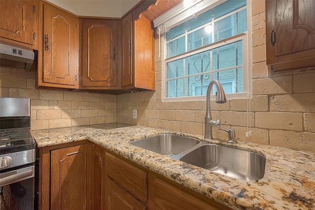 kitchen with backsplash, light stone countertops, sink, and stainless steel stove