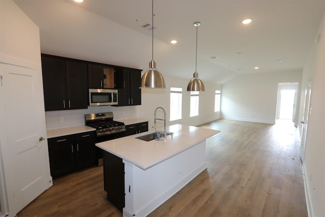 kitchen featuring appliances with stainless steel finishes, decorative light fixtures, an island with sink, lofted ceiling, and sink