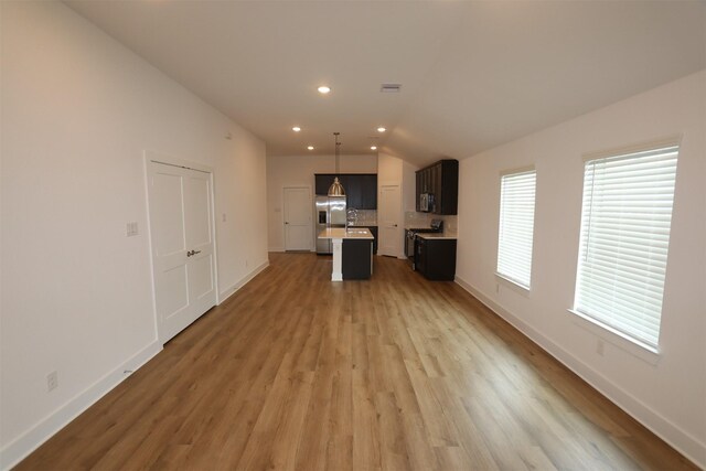 unfurnished living room featuring baseboards, a sink, wood finished floors, and recessed lighting