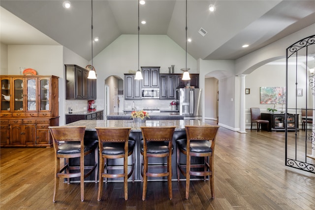 kitchen with a large island, stainless steel appliances, light stone countertops, and hardwood / wood-style floors