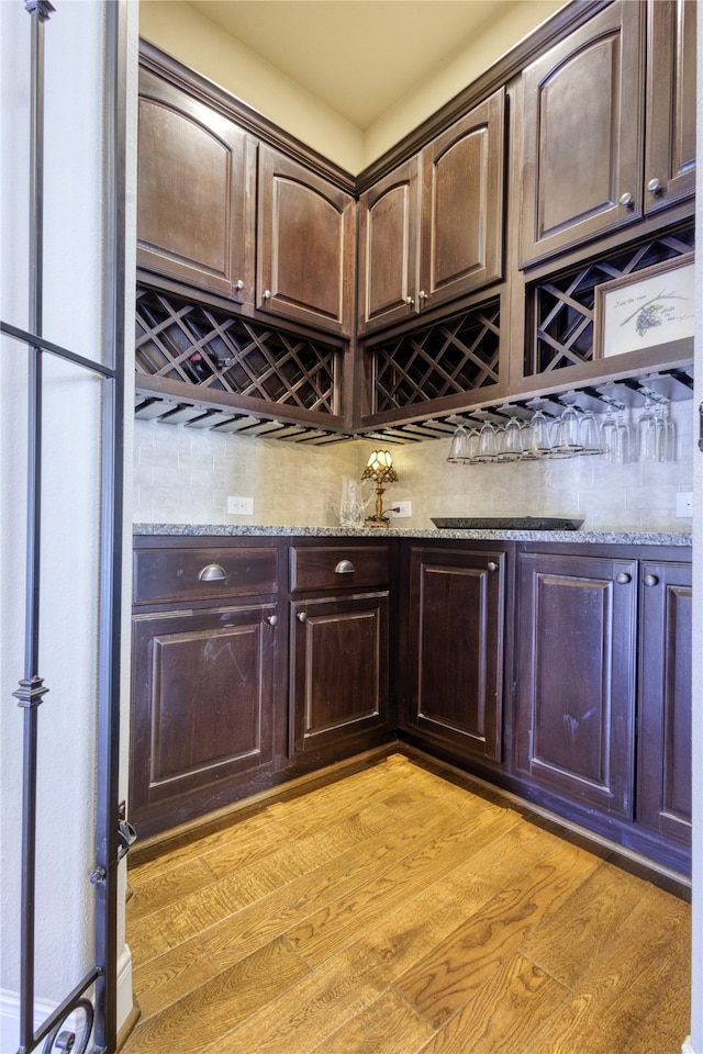 bar featuring light stone counters, light hardwood / wood-style flooring, and dark brown cabinetry