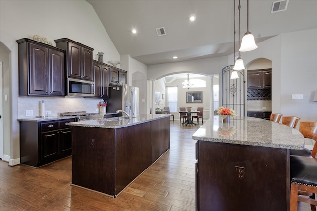 kitchen with stainless steel appliances, a center island with sink, hardwood / wood-style floors, a breakfast bar, and dark brown cabinetry