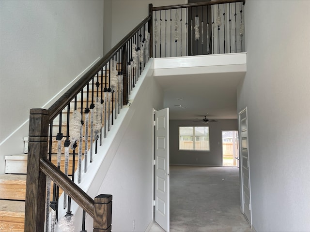 staircase with concrete flooring, a towering ceiling, and ceiling fan