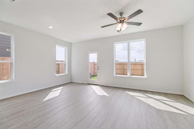 empty room featuring a ceiling fan, wood finished floors, baseboards, and a wealth of natural light