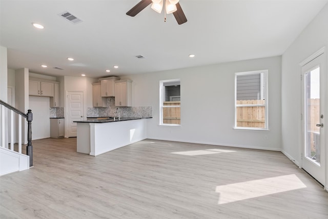 kitchen featuring visible vents, light wood-style flooring, dark countertops, a peninsula, and decorative backsplash