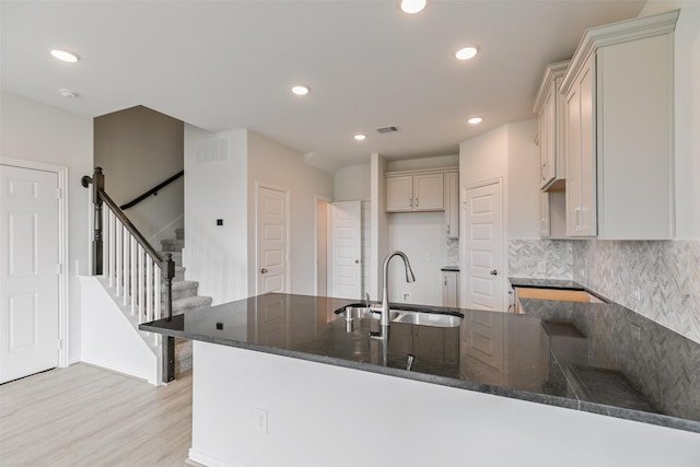 kitchen featuring light wood finished floors, a peninsula, dark stone counters, a sink, and backsplash