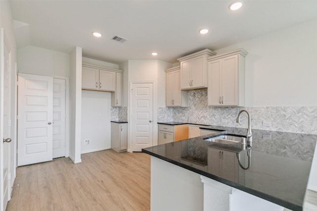 kitchen featuring visible vents, a sink, light wood-style floors, a peninsula, and decorative backsplash