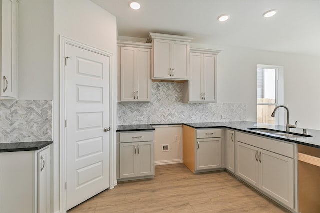 kitchen featuring dark countertops, backsplash, recessed lighting, light wood-style flooring, and a sink