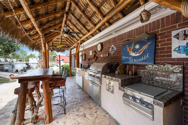 view of patio / terrace with ceiling fan, an outdoor kitchen, a gazebo, a grill, and an outdoor bar