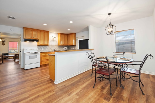 kitchen featuring kitchen peninsula, black refrigerator, backsplash, a chandelier, and white electric stove