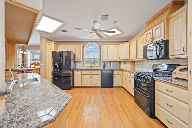 kitchen with a skylight, light brown cabinetry, and black appliances