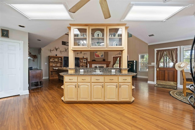 kitchen with a wealth of natural light, light brown cabinets, kitchen peninsula, and dark stone counters